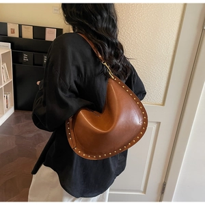 Detail view of brown leather crescent bag with gold stud rivets and wide shoulder strap
