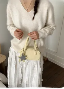 Detail of light beige bowling bag with star pendants shown on a model in a soft knit sweater