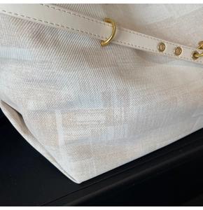 Detailed close-up of a white canvas tote with subtle monogram texture and leather straps