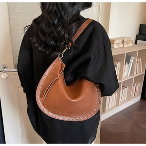 Détails du sac lune en cuir marron avec clous dorés et cordon à pompons