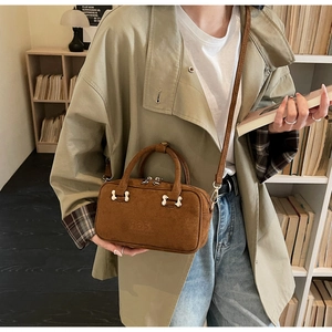 Detailed macro of coffee brown suede baguette bag with embossed logo and metal hardware