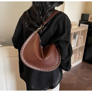 Detail of a brown leather crescent shoulder bag with gold studs and a tassel zipper