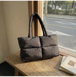 Detail of black quilted down puffer tote bag showing the soft texture on a wooden bench