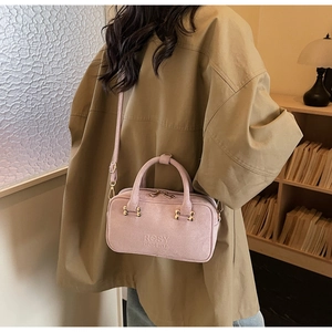 Detail of mauve suede baguette bag with brand logo and gold hardware on a leather strap