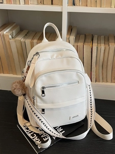White pebbled leather multi-pocket backpack with woven straps and plush charm