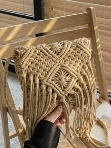 Bolso bandolera de macramé beige con flecos bohemios y patrones geométricos en una silla