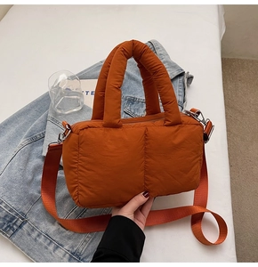 Detail of orange puffer tote bag with quilted nylon texture and silver metal buckles