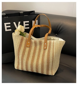 Détail d'un sac cabas tissé avec anses en cuir marron et rayures sur canapé noir