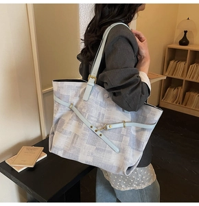 Detail of blue textured tote bag featuring leather side straps and golden hardware buckles