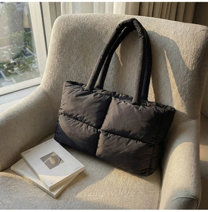 Detail view of black quilted puffer tote bag on a soft fabric chair with magazine