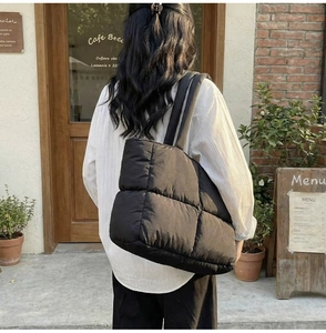 Outdoor shot of a large black quilted tote bag with wide straps on a striped shirt