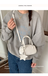 White mini Boston bag with star charm shown on a model with a casual grey outfit