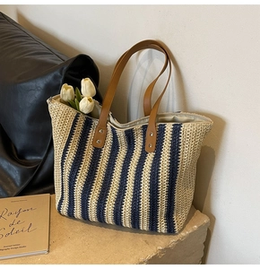 Detailed view of woven straw tote bag with navy vertical stripes and leather handles