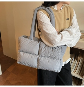 Quilted puffer tote bag in grey styled with thick shoulder straps in a cozy indoor setting