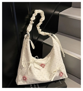 Detail of white polka dot canvas tote bag featuring red floral charms and ruffled strap