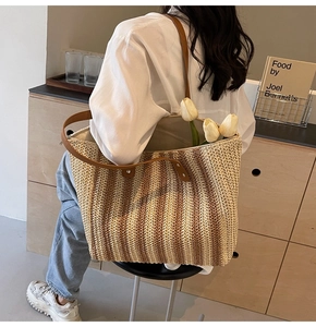 Close-up of woven straw tote bag with vertical stripes and brown leather shoulder straps