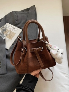 Braune gefaltete Beuteltasche mit Plüsch-Anhänger auf einem schicken grauen Blazer