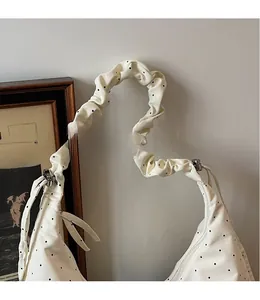 Close-up of a white polka dot half-moon bag with a unique ruched ruffle strap detail
