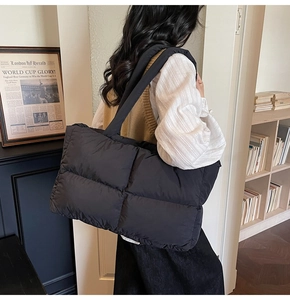 Close-up of a large black quilted tote bag with a soft puffer texture and wide shoulder strap