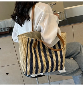 Detail of striped straw tote bag featuring brown leather straps and metal rivets