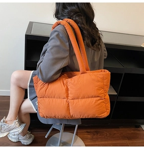 Macro shot of orange quilted puffer tote bag highlighting soft texture and padded strap