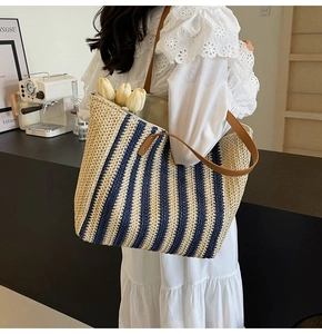 Straw tote bag detail with navy stripes and brown shoulder strap on a model
