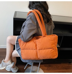 Detailed close-up of large orange quilted puffer tote bag with thick padded handles
