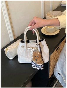 Detail der cremefarbenen Beuteltasche mit strukturierter Optik und Plüschbär-Anhänger