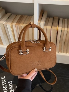 Brown matte baguette bag with silver bone buckle shown by a model against bookshelves
