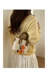 Detail of woven bucket bag with leather handles and orange horse charm on a model