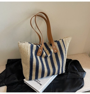 Close-up of woven straw tote bag featuring blue stripes and brown leather straps