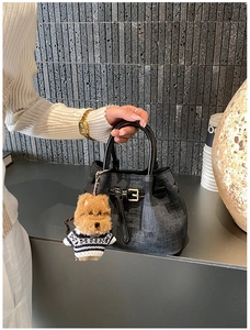 Detail der dunkelgrauen Denim-Eimertasche mit Welpenanhänger und schwarzen Lederriemen