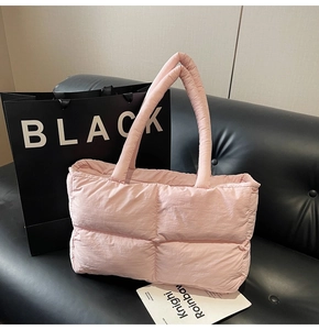 Pink quilted puffer tote bag on a black leather sofa with a minimalist paper shopping bag