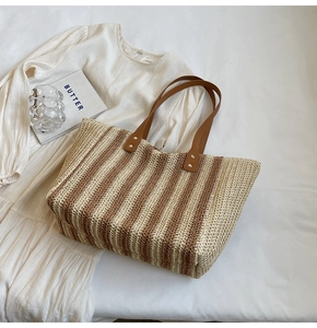 Flat lay of large straw tote bag with vertical stripes and leather handles on white bedding