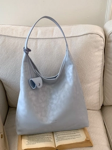 Elegant light blue hobo tote bag in textured leather with knot detail on sofa