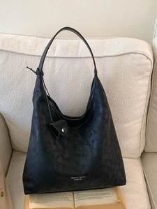 Large black minimalist tote bag with small pouch displayed on a white sofa with books