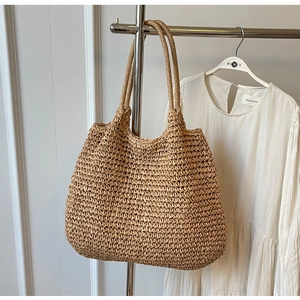 Primo piano di una grande borsa tote in paglia intrecciata su un espositore minimalista