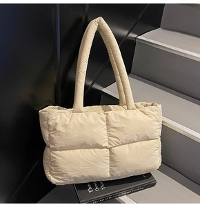 Detailed view of beige quilted puffer tote bag on a staircase with stylish book