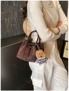 Detail der braunen Vintage-Eimertasche mit Teddybär-Anhänger und Metallschnalle