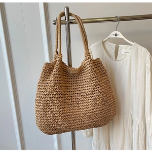 Dettaglio di una borsa tote in paglia naturale appesa con un abito bianco estivo