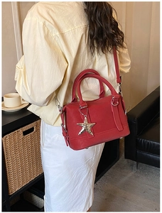 Red leather Boston bag with star pendant shown worn over the shoulder by a model
