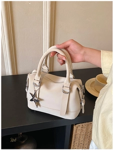 Detail of a creamy white Boston bag with silver star charm and smooth PU leather finish