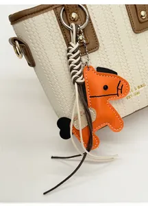 Detail of orange leather horse charm with woven cord on a white textured handbag