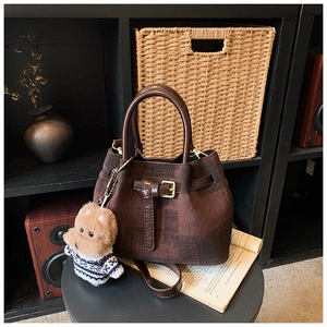 Detail einer braunen Tweed-Eimertasche mit Lederriemen und einem süßen Welpen-Anhänger