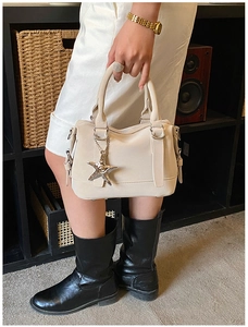 Close-up of cream Boston handbag featuring a silver star charm and textured leather finish