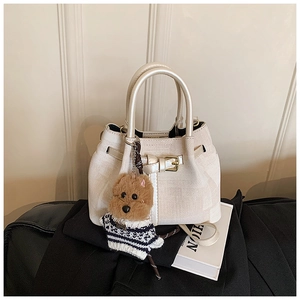Detail der cremeweißen Web-Eimertasche mit Goldschnalle und niedlichem Hunde-Plüschanhänger