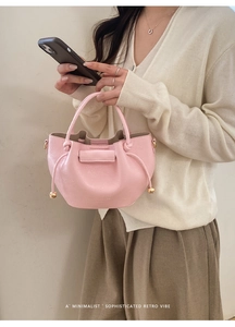 Detail der rosa gerafften Beuteltasche mit goldener Kugelverzierung am Model