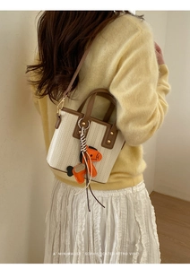 Detail of woven bucket bag with brown leather trim and a horse leather charm