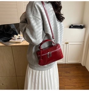 Détail du sac boîte en cuir brillant rouge foncé avec zip argenté porté par un mannequin