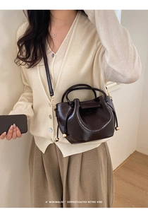 Retro dunkelbraune Lackleder-Eimertasche mit Goldkugel-Akzent an einem Modell